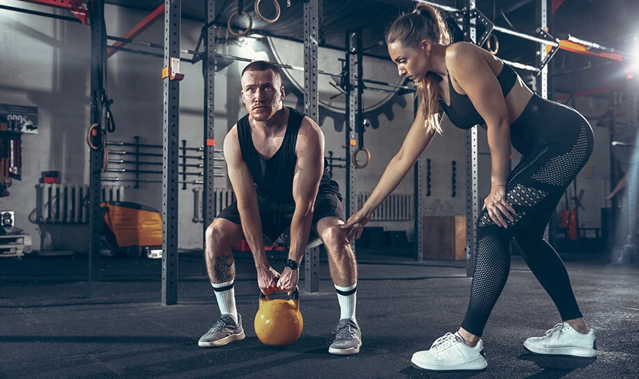 Athlete practicing a kettlebell lift with a coach in a functional fitness gym